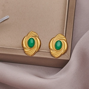 Detailed close-up of vintage gold earrings with oval green stones on soft silk fabric