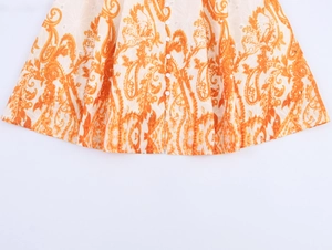 Dettaglio di abito arancione con stampa paisley ricamo traforato e bottoni bianchi