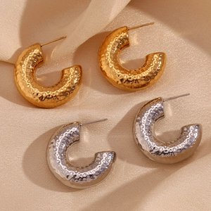 Macro detail of gold and silver hammered hollow hoop earrings on champagne silk fabric