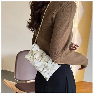 Detail of white envelope clutch bag with gold snake skin texture and metal chain