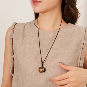Detail of a brown tiger eye heart pendant on a black woven cord necklace on a model