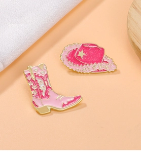 Detail of pink enamel cowboy boot and hat brooches with 'Let's go girls' text and glitter finish