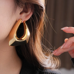Close-up of a large chunky gold geometric earring worn by a model in a high-fashion shot