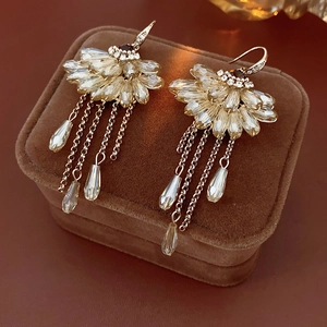 Detailed view of fan-shaped crystal tassel earrings with gold chains on brown velvet box