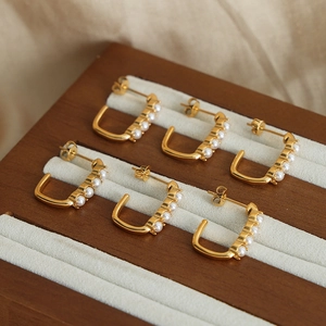 U-shaped gold plated titanium steel earrings with white pearls on a velvet display stand