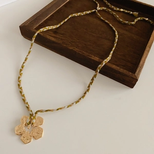 Detail shot of golden flower pendant with hammered texture on a colorful braided cord