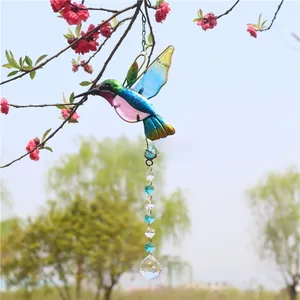 Detail of a colorful hummingbird crystal suncatcher hanging from pink flowers in a garden