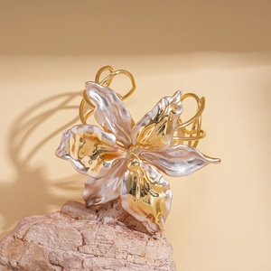 Detailed close-up of textured two-tone metal flower petal cuff bracelet on stone base