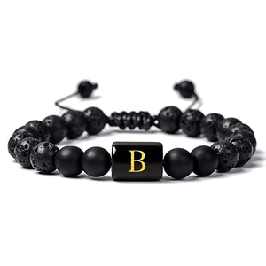 Détail de bracelet en pierre de lave noire avec perle dorée lettre B et cordon tressé