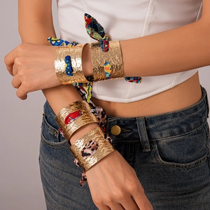 Dettaglio di bracciali a polsino martellati in oro intrecciati con sciarpe di seta colorate