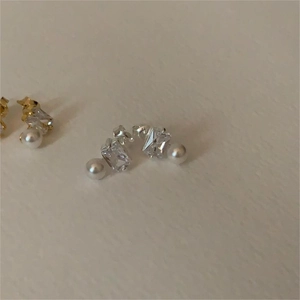 Detail of square zircon and pearl drop earrings in gold and silver finish minimalist style