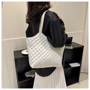Détail du grand sac cabas blanc matelassé porté par un mannequin dans un studio minimaliste