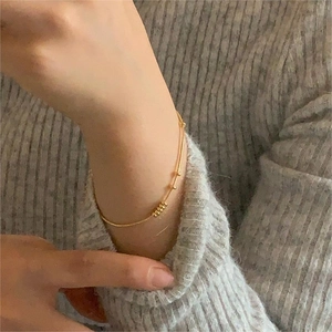 Detail of a thin gold snake chain bracelet with five beads on a grey knit sleeve