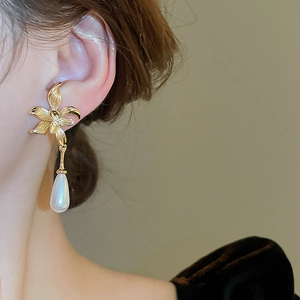 Detail view of flower-shaped earrings with teardrop pearls worn by a model in warm light