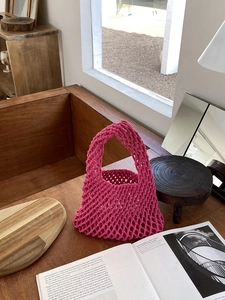 Detail of rose red cotton rope woven tote bag placed on a rustic wooden table by the window