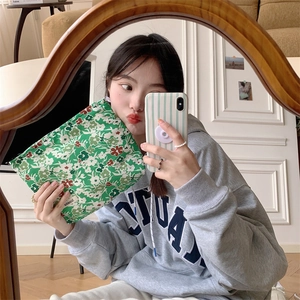 Detailed view of a green floral cotton makeup bag held by a person in a mirror selfie