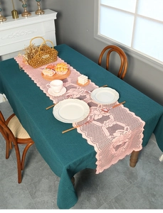 Close-up of pink lace table runner with hollow crochet over dark green linen tablecloth