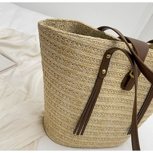 Detail of hand-woven beige straw tote with brown leather straps and gold hardware accents