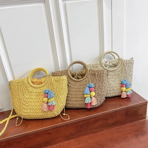 Three bohemian straw handbags with round handles and colorful tassel charms on wooden steps