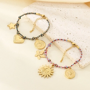 Detail of bohemian hand-woven bracelets with golden heart and sun pendants on white stone