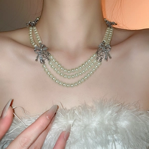 Detailed view of layered pearl necklace with shimmering diamond bow clasp on neck
