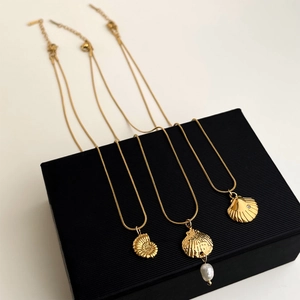 Detailed shot of three gold shell necklaces with pearl accents on a black jewelry box
