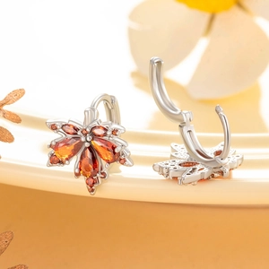 Silver maple leaf earrings with orange zircons on a beige background with soft bokeh