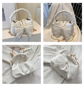 Detail view of white ruched handbag featuring large bow design and gold chain strap