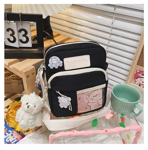 Détail du sac bandoulière en toile noire avec poche PVC et écussons de dessin animé