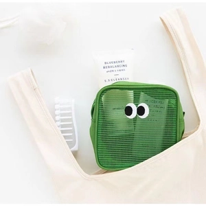 Dettaglio trousse a rete verde con occhi buffi posta in una borsa tote beige