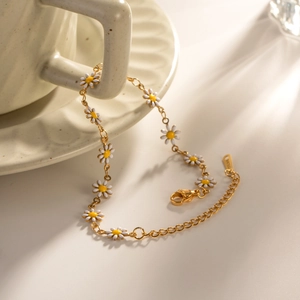 Close-up of golden stainless steel bracelet with white daisy charms on ceramic cup
