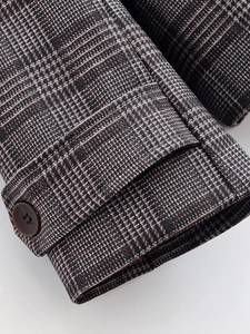 Detail view of plaid jacket sleeve cuff with a dark brown four-hole button and textured fabric