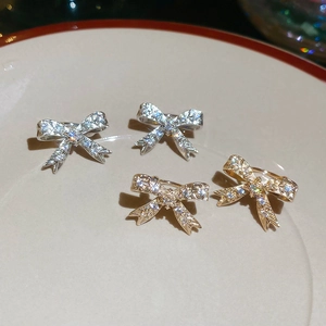 Dettaglio di ear cuff a fiocco in oro e argento con zirconi lucidi su vassoio di ceramica