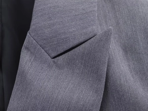 Gros plan du revers d'un blazer gris montrant la texture du sergé et les surpiqûres