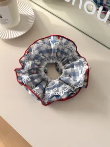 Detail view of blue plaid hair scrunchie with lace embroidery on a cream surface