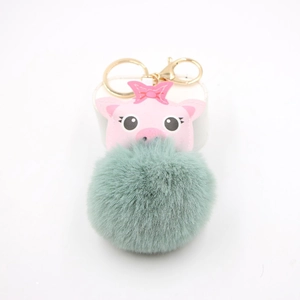 Detail of pink pig plush keychain with green pompom and gold hardware on white background