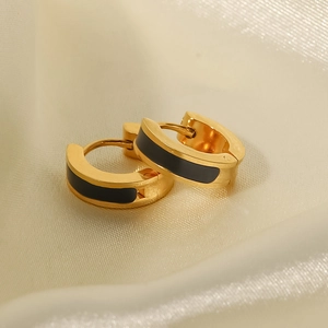 Close-up of gold and black hoop earrings on a beige silk texture background