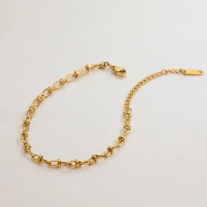 Macro detail of gold link chain featuring textured oval rings and lobster clasp closure