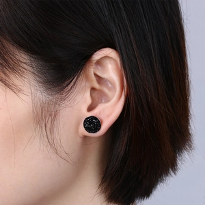 Close-up of black druzy round stud earring with shimmering texture on model's ear