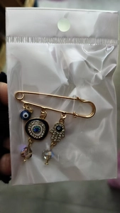Macro detail of gold safety pin brooch with blue evil eye and crystal Hamsa hand charms