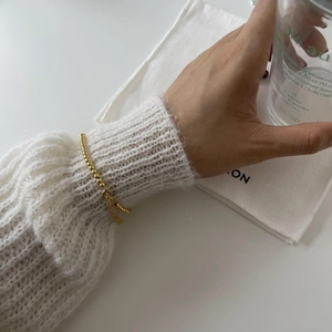 Detail shot of a minimalist gold beaded bracelet on a wrist with a soft mohair sweater