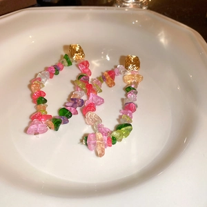 Detail of colorful gravel tassel earrings on white ceramic plate with soft warm lighting