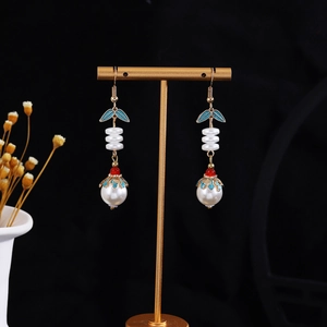 Detail of hanging butterfly pearl tassel earrings with blue enamel leaves on gold stand