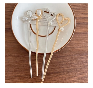 Detailed shot of gold and silver pearl hairpins with heart and leaf designs on a ceramic dish