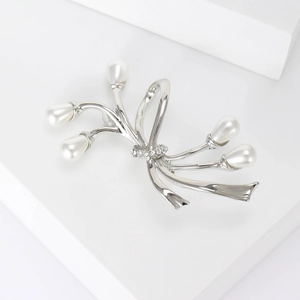 Détail macro d'une broche florale argentée avec cinq perles blanches et strass brillants