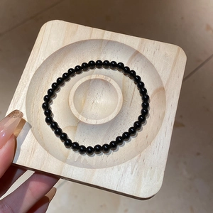 Close-up of polished black obsidian beaded bracelet on a natural wooden display tray