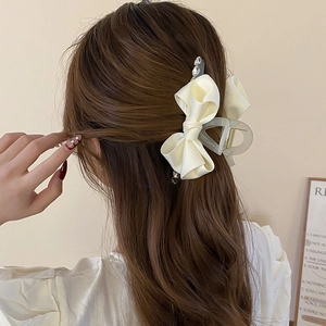 Detail of elegant beige satin bow hair claw clip with rhinestones worn by a model