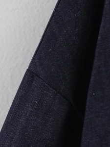 Detailed close-up of heavy dark blue denim fabric texture and stitching of the jacket