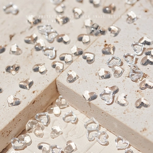 Transparent heart-shaped nail art charms scattered on a textured stone surface