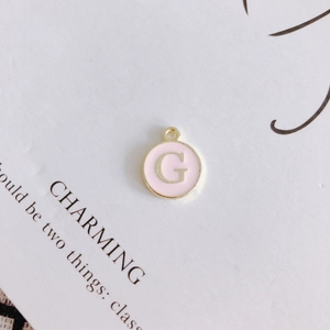 Detailed macro of a round pink enamel G letter pendant with golden metal edging and ring